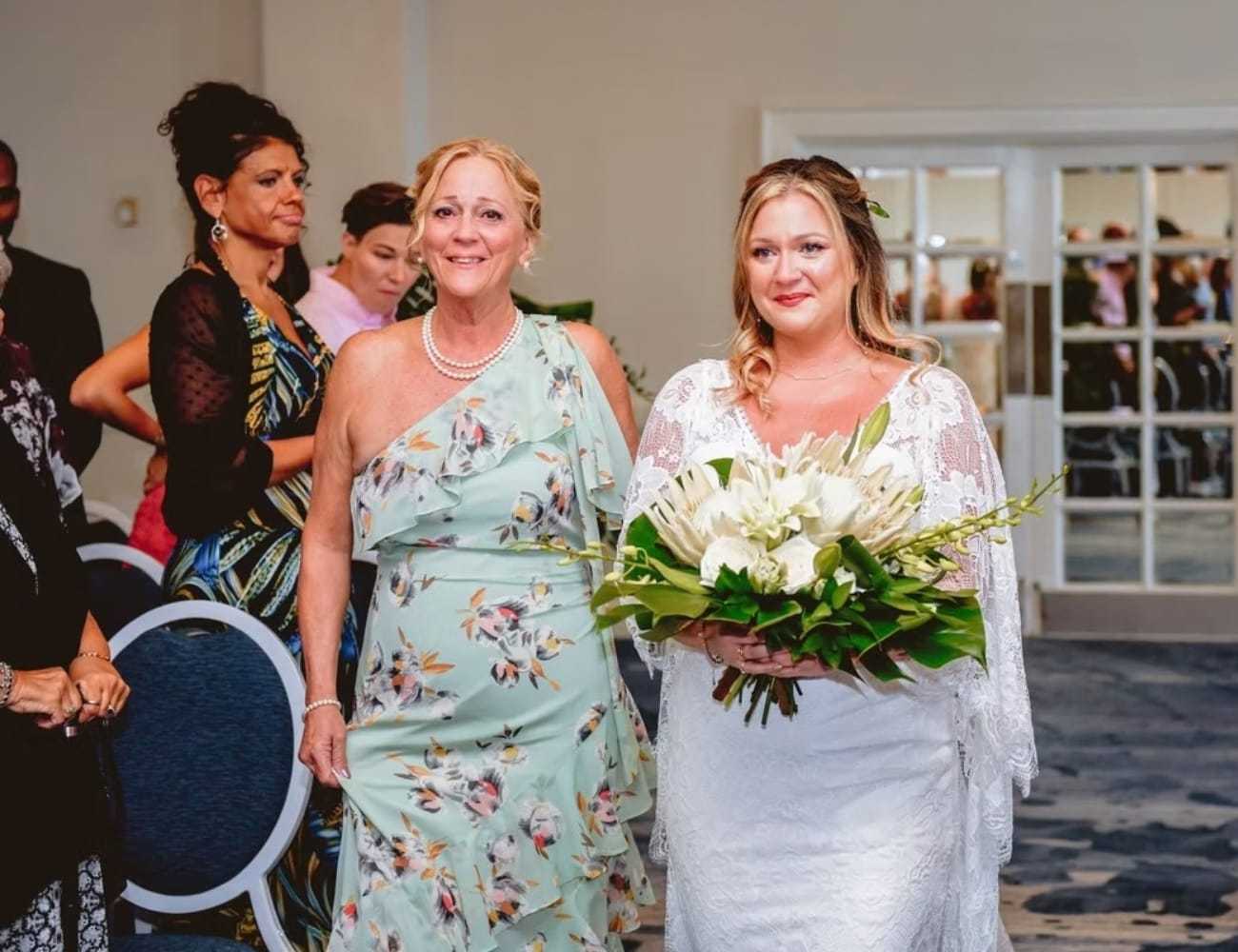 Bride and mother walking down the aisle, holding a bouquet, in a wedding ceremony.